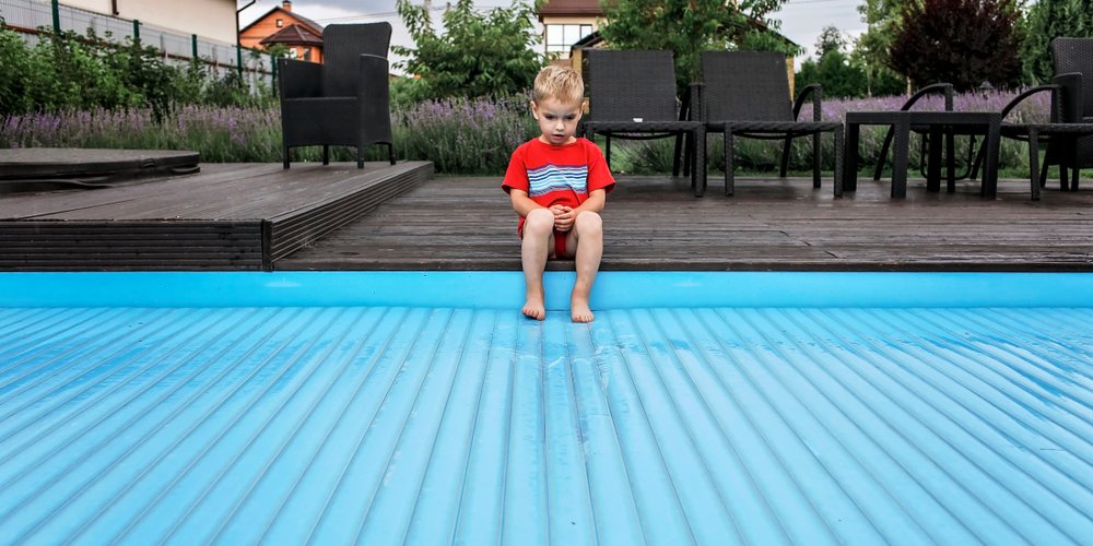 little boy sitting on side of pool with feet on pool cover