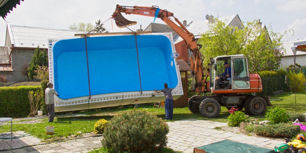 digger with wheels carrying a fiberglass pool