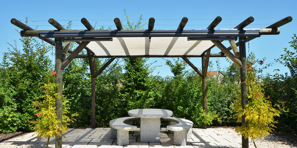 seat and table under a pegola with a plant hedge