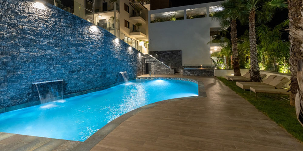 big stone wall in front of a pool with undercap lights on it