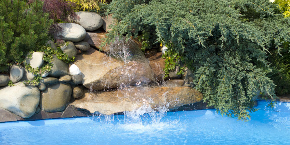 stone waterfall cascading into a swimming pool