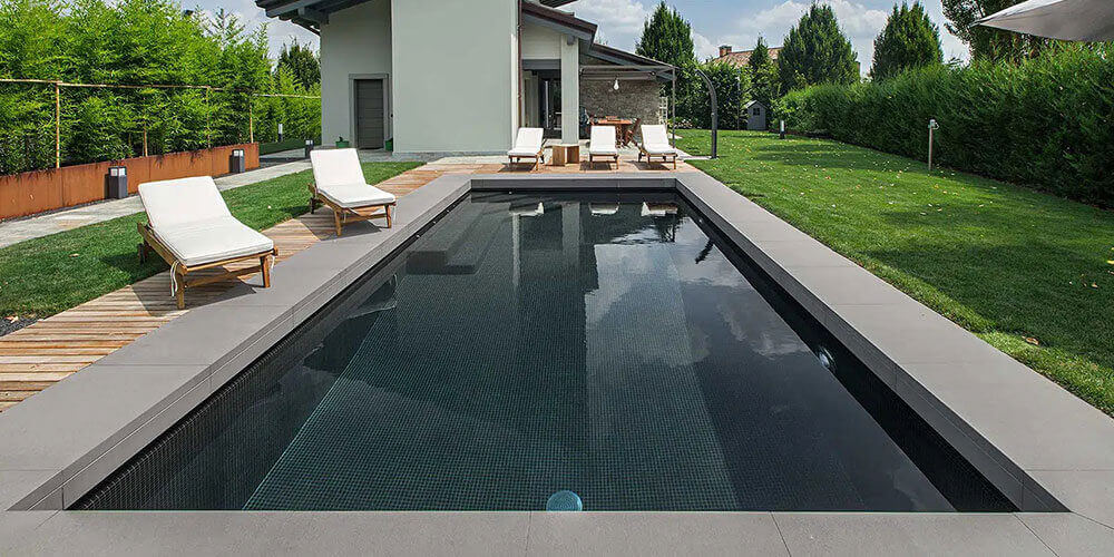 dark bottomed pool with grey tiles and concrete coping