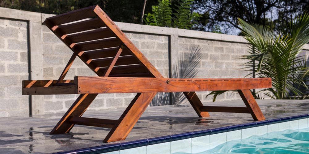 wooden sun lounger chair standing in a green garden by the side of a swimming pool