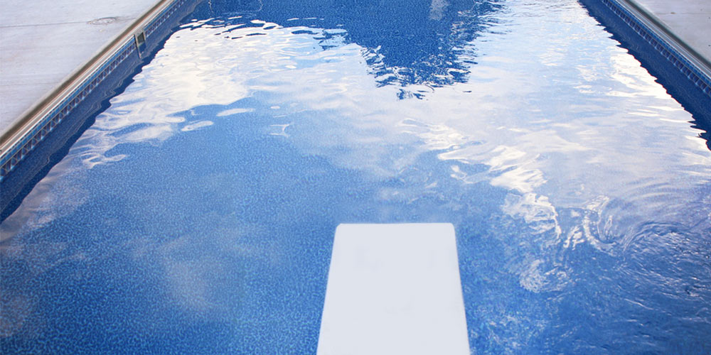 a pool without any people in it with a diving board and reflections of clouds