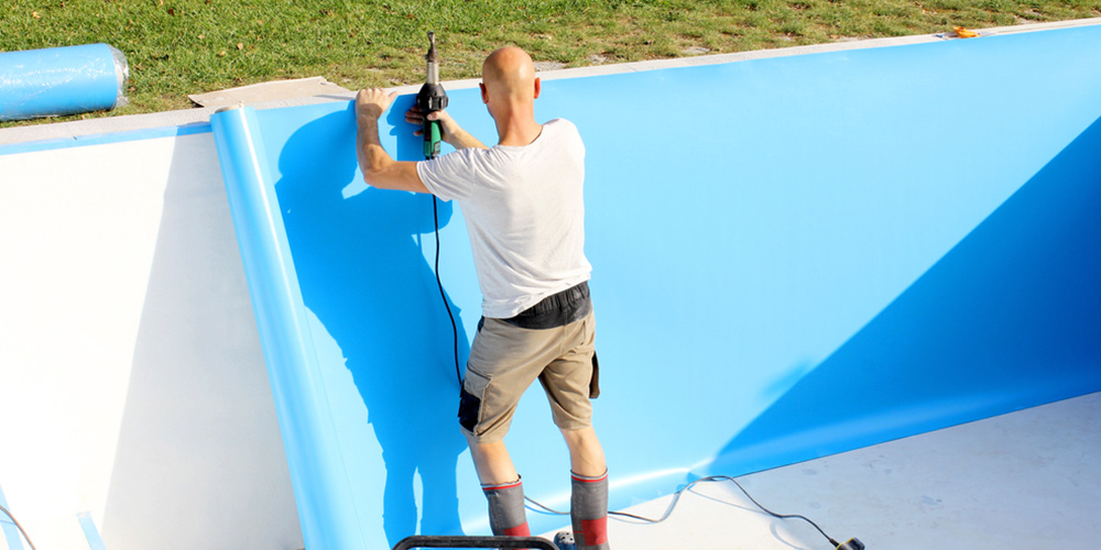 A man is working on a blue pool wall.
