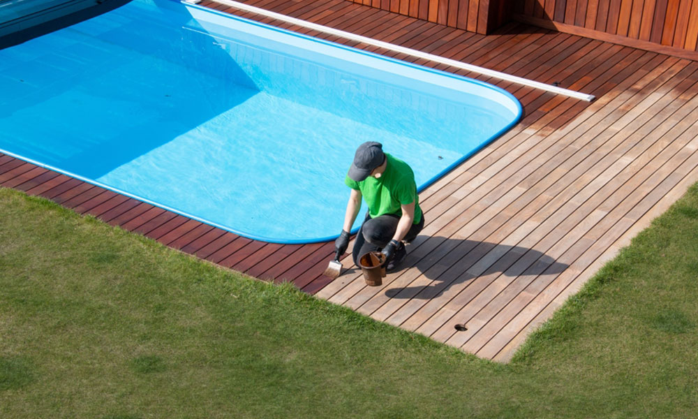 person applying refreshing coat to poolside wood decking