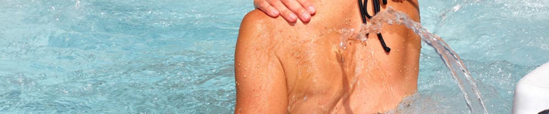 A person in a black swimsuit sitting in a bubbling hot tub, with water jets massaging their back.