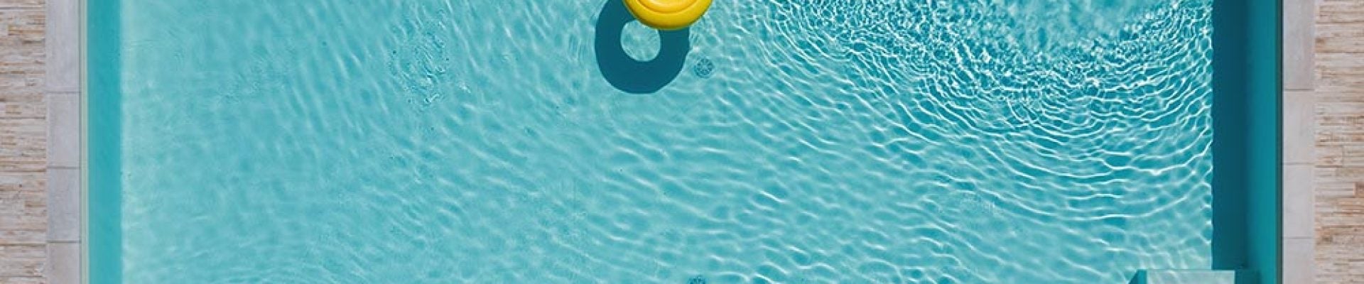 Aerial view of a rectangular swimming pool with a single yellow pineapple-shaped float, surrounded by a tiled deck with several lounge chairs.
