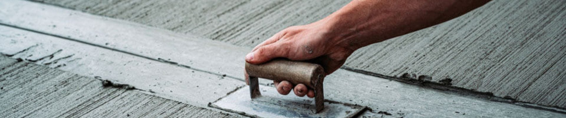 A person smoothing wet concrete with a hand trowel, focusing on the arm and hand in action.