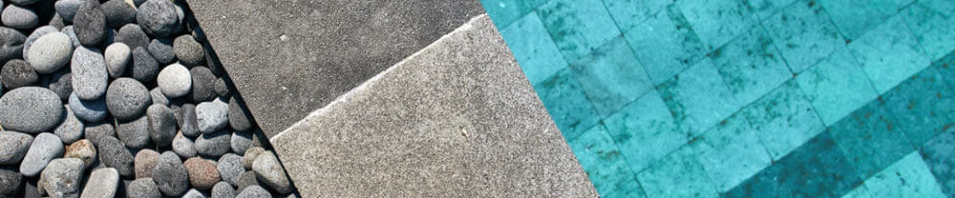 Close-up view of pebbles, concrete tiles, and a turquoise pool with a tiled bottom, divided by the concrete edge of the pool.