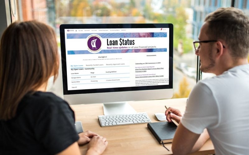 Two people sitting at a desk look at a computer screen displaying a "Loan Status" webpage with details about financed projects.