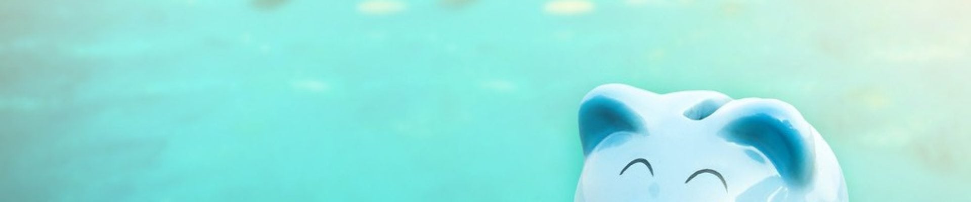 A blue piggy bank with pink cheeks sits on a wooden surface with a blurred turquoise background.
